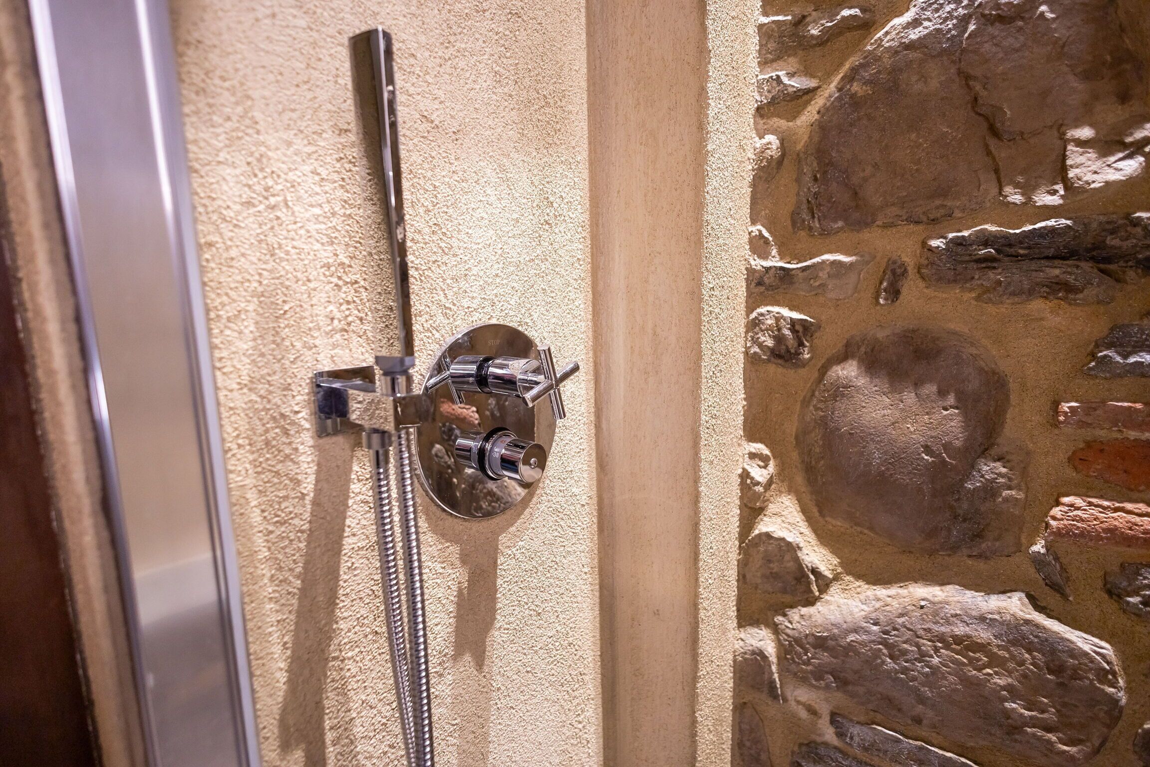 A shower with a stone wall and a metal door frame.
