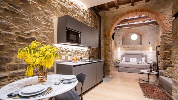 Eine moderne Küche mit Steinwänden, ein Essbereich mit Tisch für zwei Personen und ein Schlafzimmer mit Bett und Nachttisch.