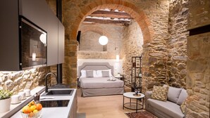 Eine moderne Küche mit einem Steingewölbe, das in ein Schlafzimmer mit einem großen Bett und einem runden Tisch führt.