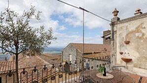 A terrace with a round metal table and chairs, a view of terracotta-roofed buildings, and a tree. - La Terrazza Sulla Valle (Cortona)
