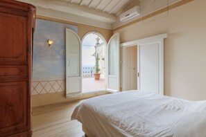 A bedroom with a large bed, a wardrobe, a mirror, and an open door leading to a balcony with a view of a building. - La Terrazza Sulla Valle (Cortona)