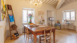 A dining area with a wooden table, chairs, a chandelier, a ladder with a basket, and a radiator. - La Terrazza Sulla Valle (Cortona)