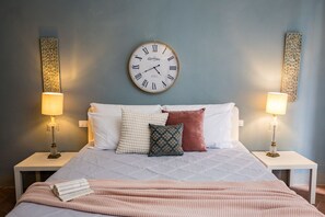 A neatly made bed with a clock, two bedside lamps, and decorative pillows. - Rose's Palace (Cortona)