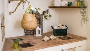 A kitchen with a rustic design, featuring a woven basket hanging, a green pot on the counter, and a shelf with decorative items. - Rose's Palace (Cortona)