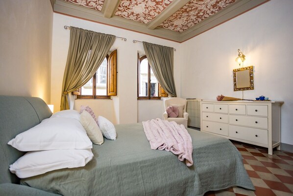 A bedroom with a bed, a dresser, a chair, and a window with curtains. - Rose's Palace (Cortona)