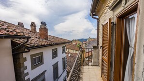 A narrow balcony with a metal railing, a white building with multiple windows, and a red-tiled roof. - Rose's Palace (Cortona)