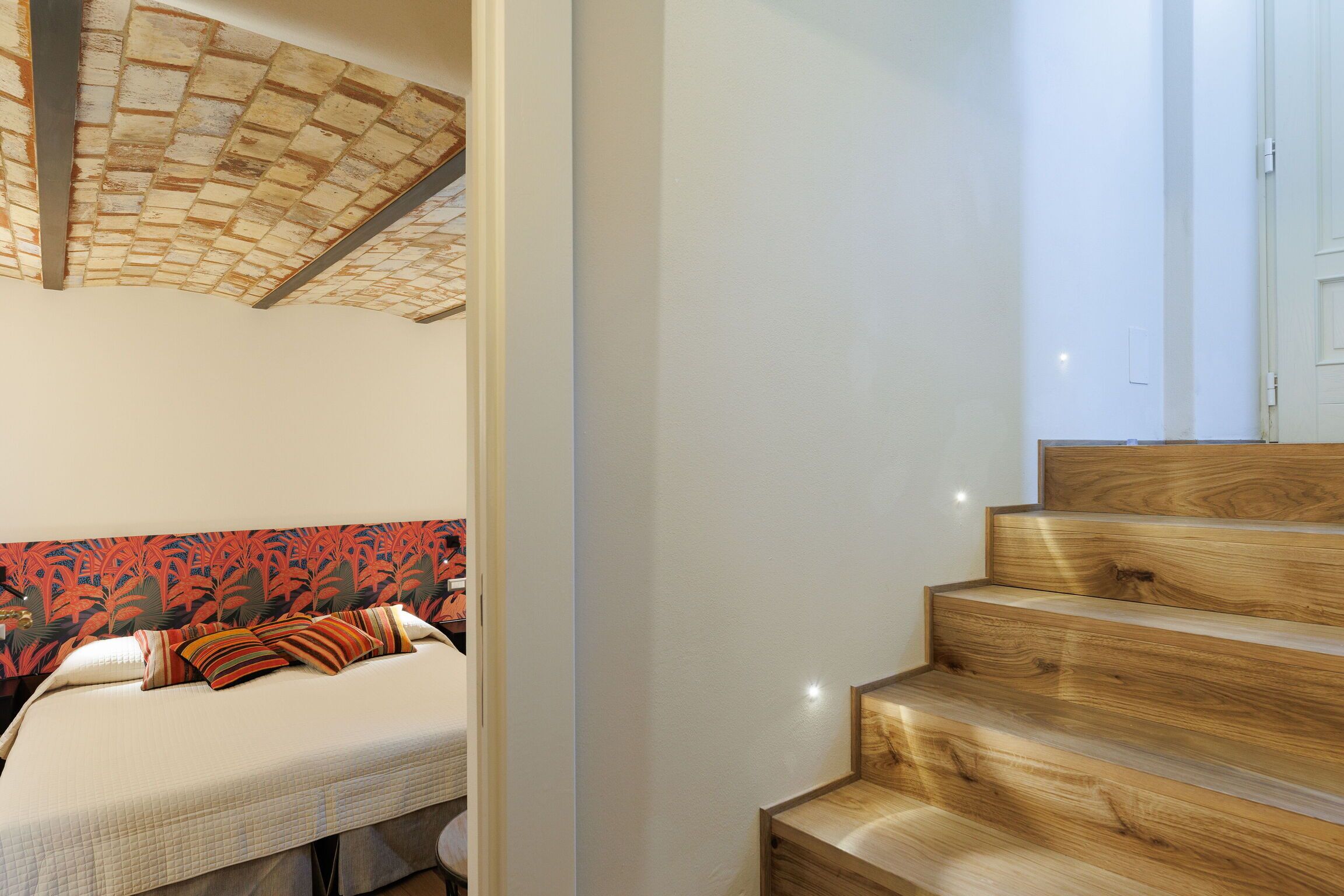A bedroom with a bed, a headboard with a red and black pattern, and a wooden staircase.