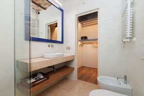 Une salle de bain moderne avec une cloison en verre, un lavabo blanc, un miroir avec un cadre bleu, une étagère en bois et une baignoire blanche.