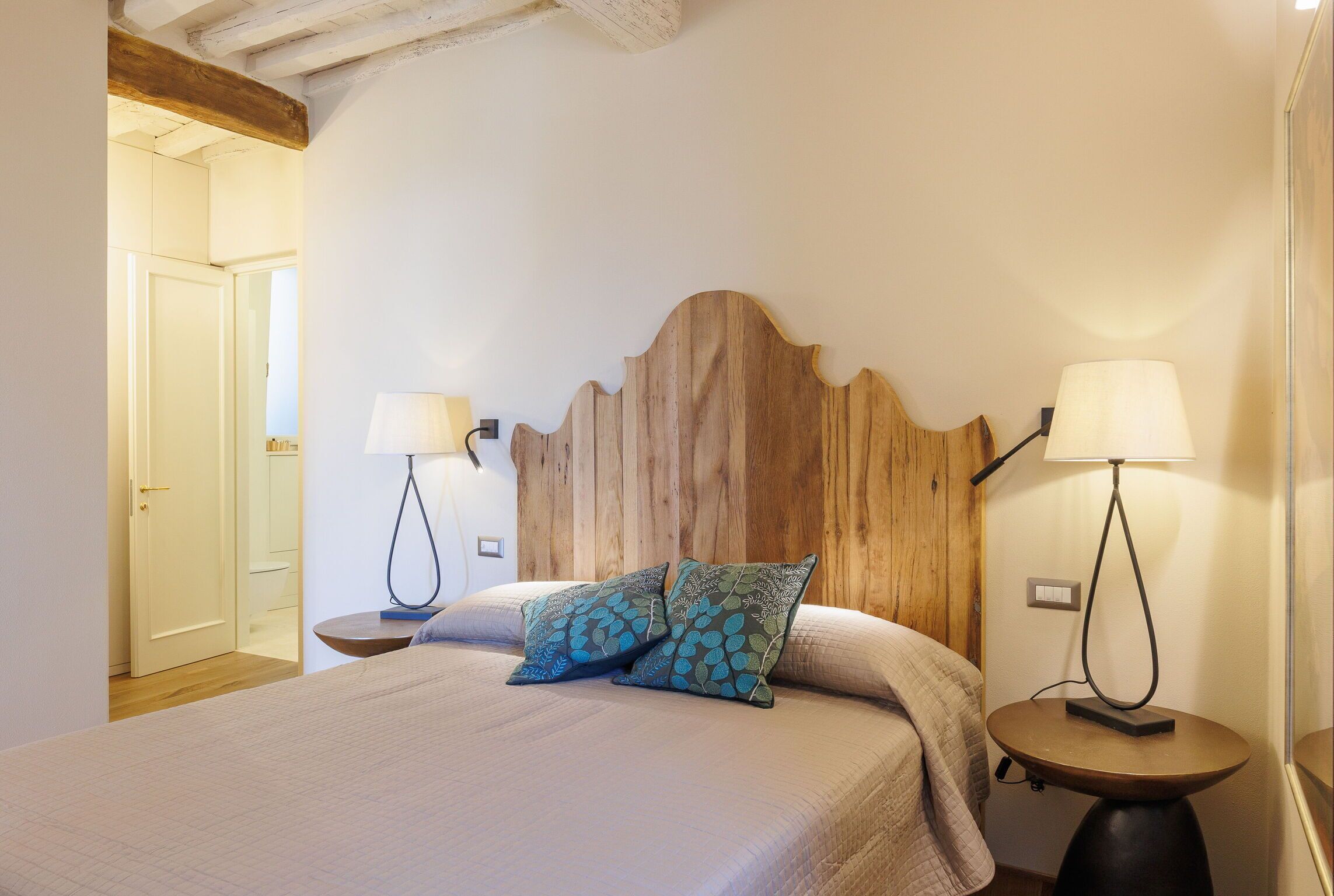A bedroom with a wooden headboard, two bedside lamps, and two patterned pillows.