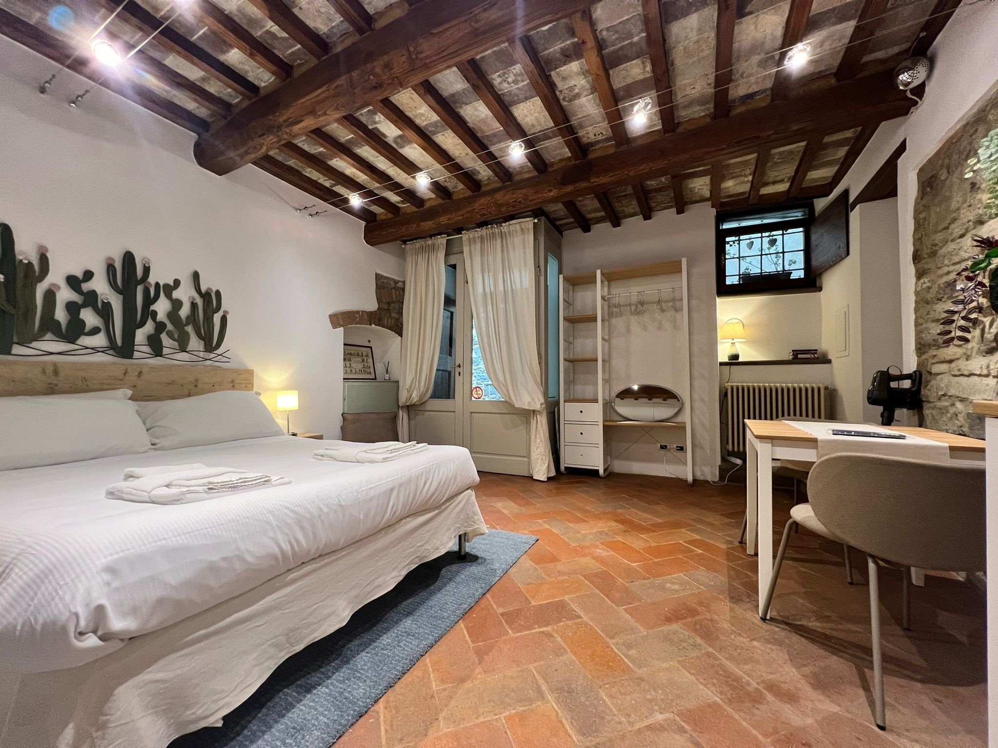 A bedroom with a bed, a desk, a chair, a radiator, and a TV on the wall.