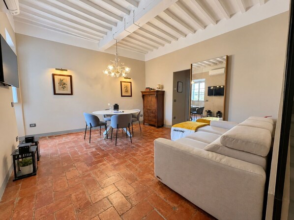 A modern living room with a sofa, a dining table with chairs, a fireplace, and a large mirror. - Via Roma 39 (Cortona)