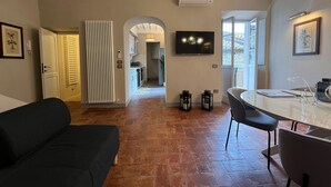 Una sala de estar moderna con un sofá negro, un área de comedor con una mesa de vidrio y una cocina al fondo.
