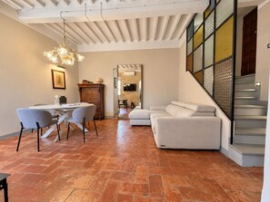 A spacious living area with a dining table, two chairs, a sofa, and a staircase with a glass railing. - Via Roma 39 (Cortona)