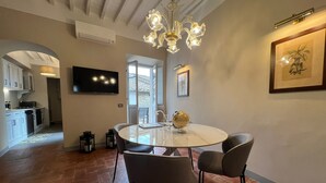 Un comedor con una mesa redonda, cuatro sillas, una araña y un televisor en la pared.