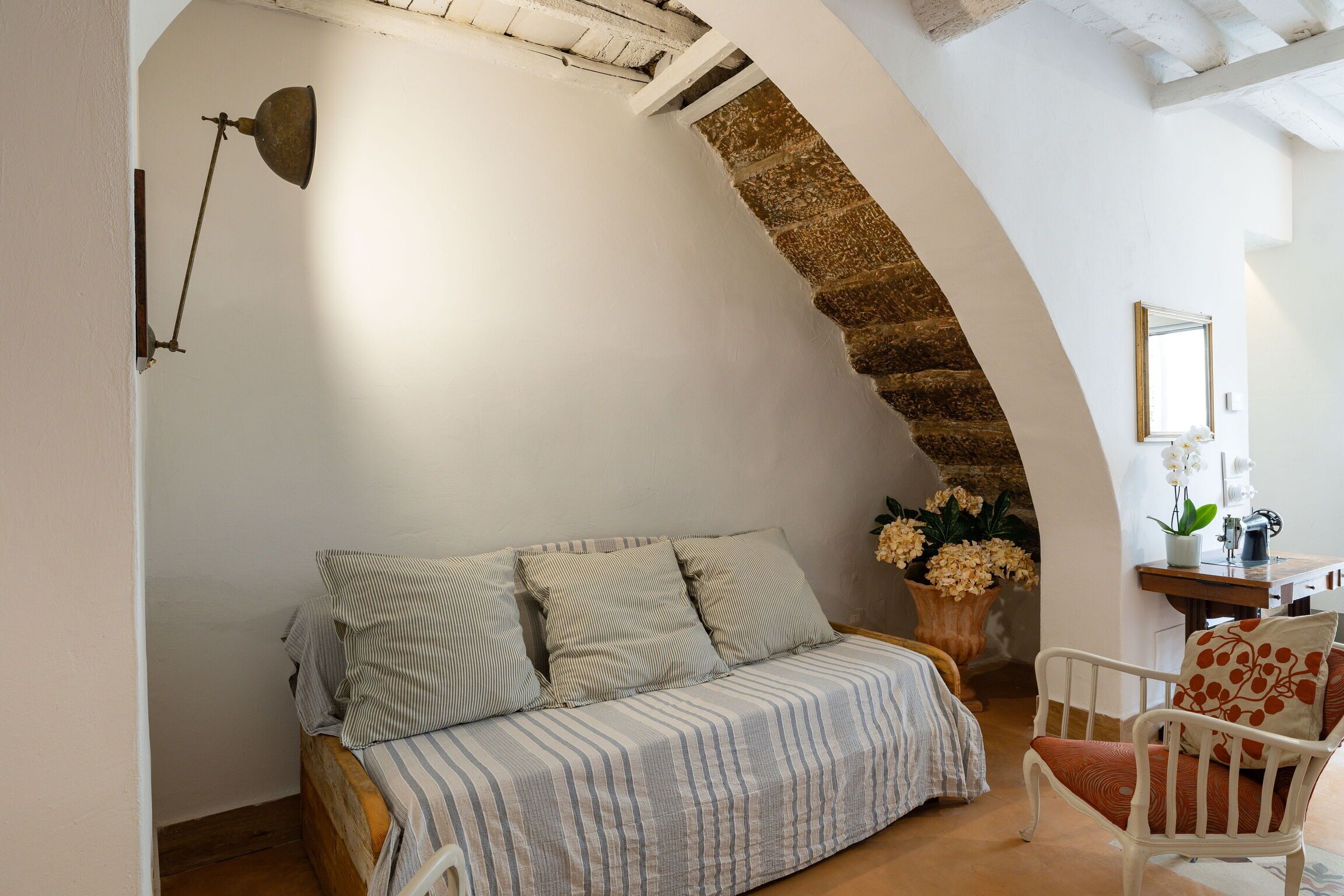 Une pièce chaleureuse avec un lit en bois, une chaise blanche, un bureau avec un miroir et une arche en pierre.