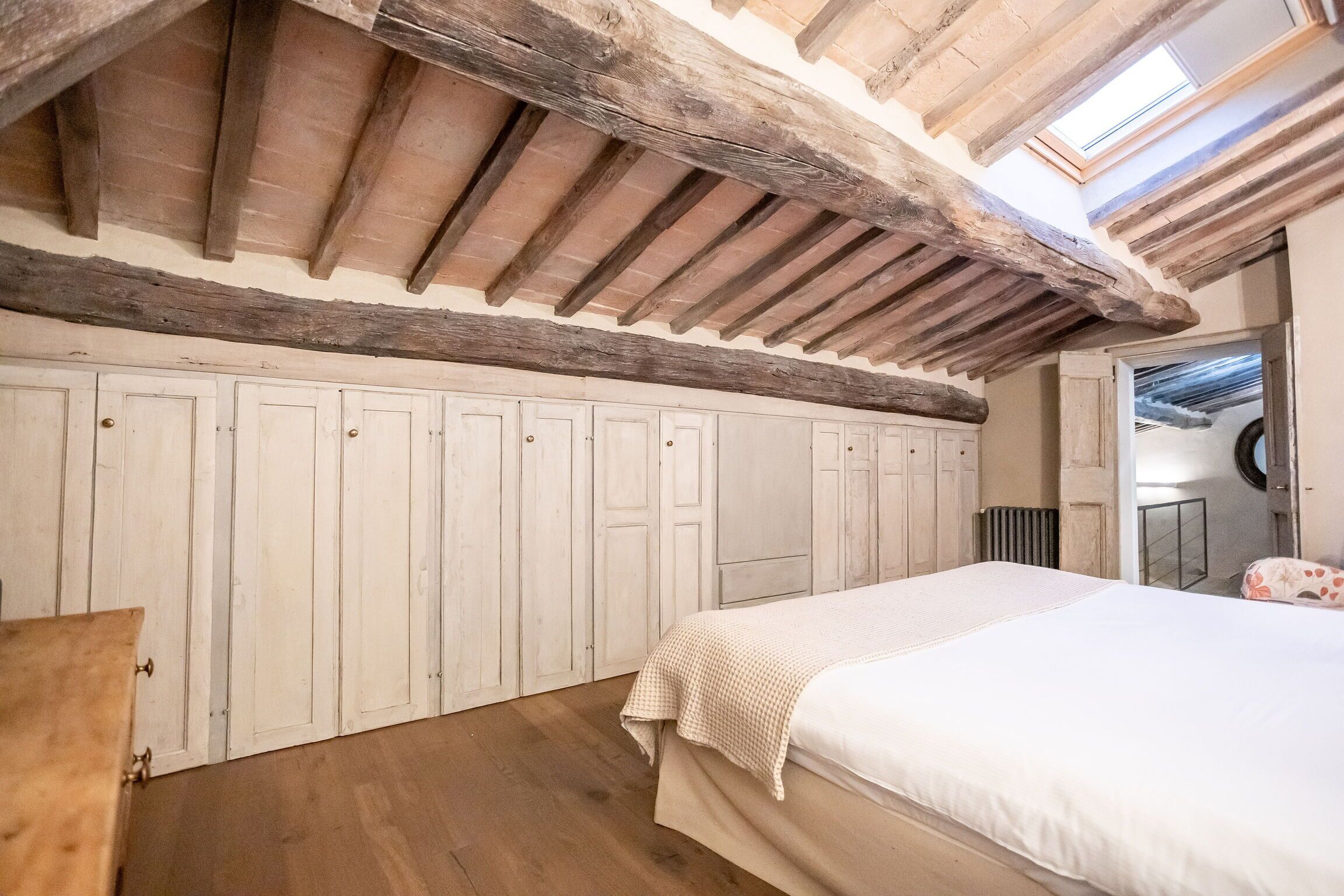 Ein Schlafzimmer mit Holzboden, weißen Wänden und einem Bett mit weißer Bettdecke.