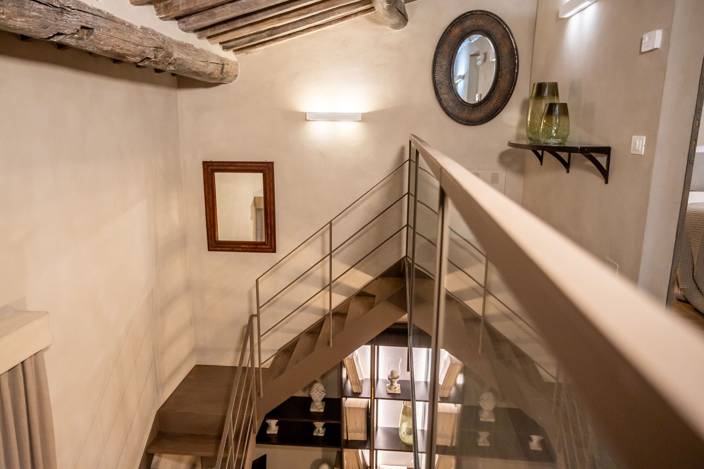 A staircase with a glass railing, a wooden ceiling beam, and a wall-mounted shelf with decorative items.