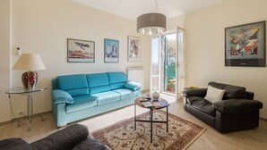 A living room with a blue sofa, a black sofa, a glass coffee table, and a patterned rug. There are framed pictures on the wall and a lamp on a side table. - Casa Maria (Cortona)