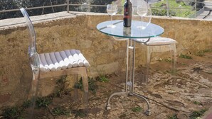A terrace with a glass table and chairs, a bottle of wine, and a view of the sea and buildings. - Casa Maria (Cortona)