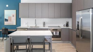 Een moderne keuken met grijze kastjes, een roestvrijstalen koelkast, een inbouwoven en een wit aanrecht.