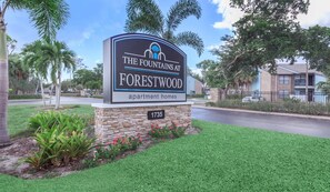 Placa para os apartamentos The Fountains at Forestwood, com base de pedra e céu azul claro ao fundo.