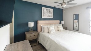 A bedroom with a bed, nightstands, a ceiling fan, a wall-mounted artwork, and a mirror. - Landing Apartments Fort Myers Near Pine Manor (Fort Myers)