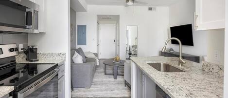 A modern kitchen with granite countertops, stainless steel appliances, and a flat-screen TV mounted above the sink.