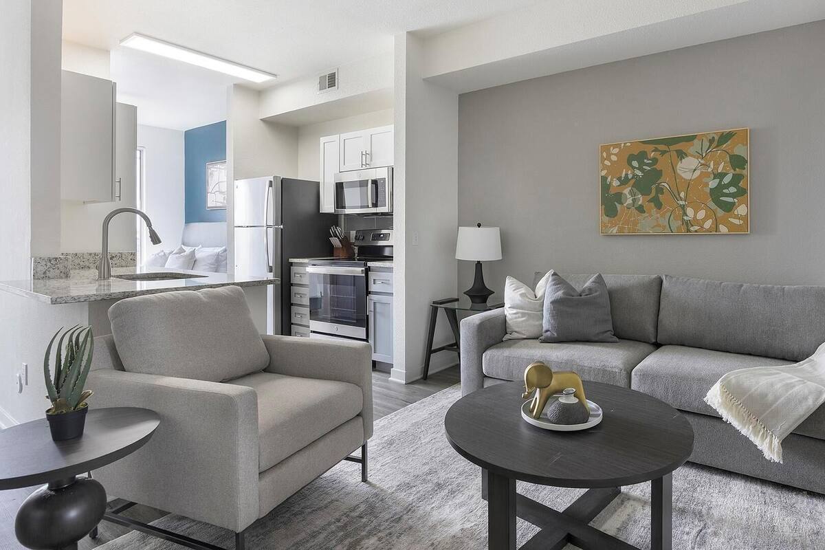 A modern living room with a grey sofa, a coffee table, and a dining area with a refrigerator and microwave.