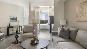 Ett modernt hotellrum med ett vardagsrum, ett matbord, en soffa, ett kök och en balkong med utsikt.