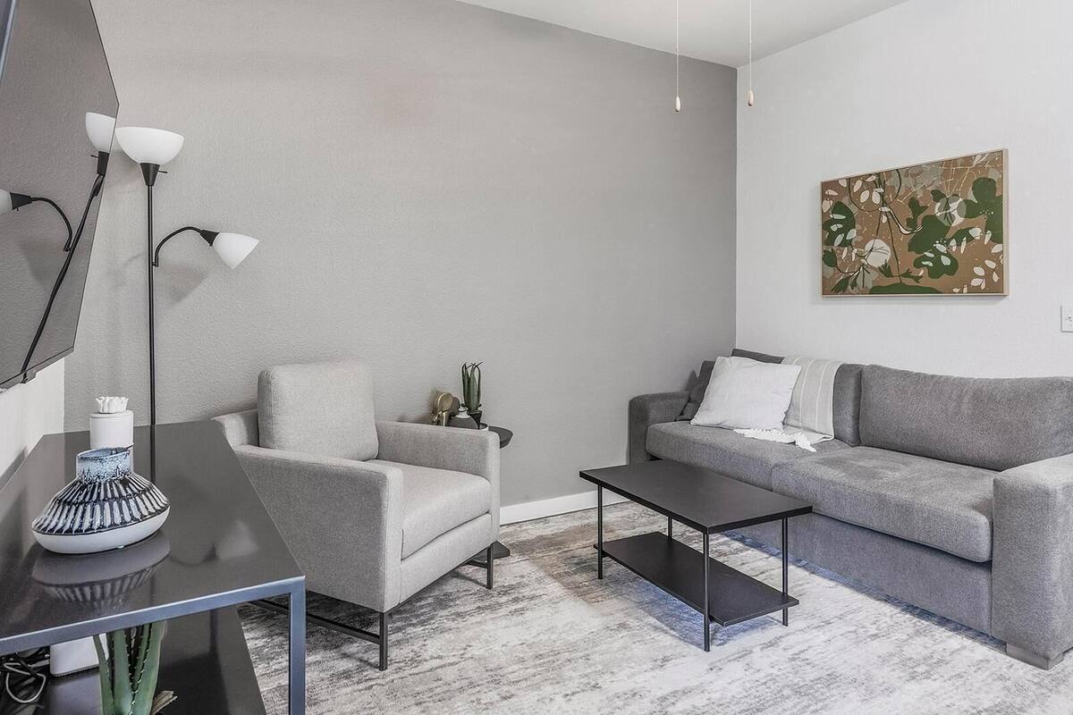 A modern living room with a grey sofa, a coffee table, a side table with a vase, a floor lamp, and a painting on the wall.