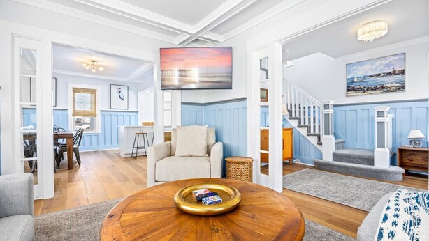 A spacious living room with a wooden coffee table, a comfortable sofa, and a TV mounted on the wall. - Spacious OC 5br + Den Steps to Beach and Boards (Ocean City)