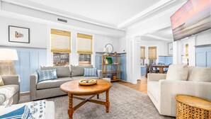 A spacious living room with a sofa, armchairs, and a coffee table. There is a dining area with a table and chairs, and a kitchen visible in the background. - Spacious OC 5br + Den Steps to Beach and Boards (Ocean City)
