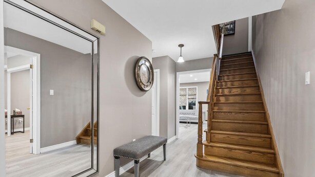 Un couloir avec un escalier en bois, un banc, un grand miroir et une horloge murale.