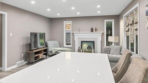 Un salon moderne avec une grande table blanche, une cheminée, un téléviseur et un coin salon confortable.