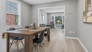 Un espace repas moderne avec une table en bois, des chaises noires et une vue sur un mur de briques à travers de grandes fenêtres.