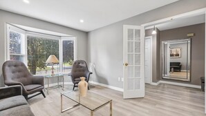 Un salon moderne avec deux fauteuils gris, une table basse en verre et une porte donnant sur une autre pièce.