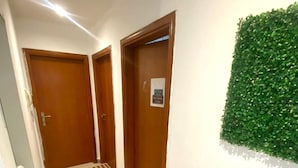 A hallway with two wooden doors, a green wall feature, and a tiled floor. - Lavish Partition Room in Tecom (Dubai)