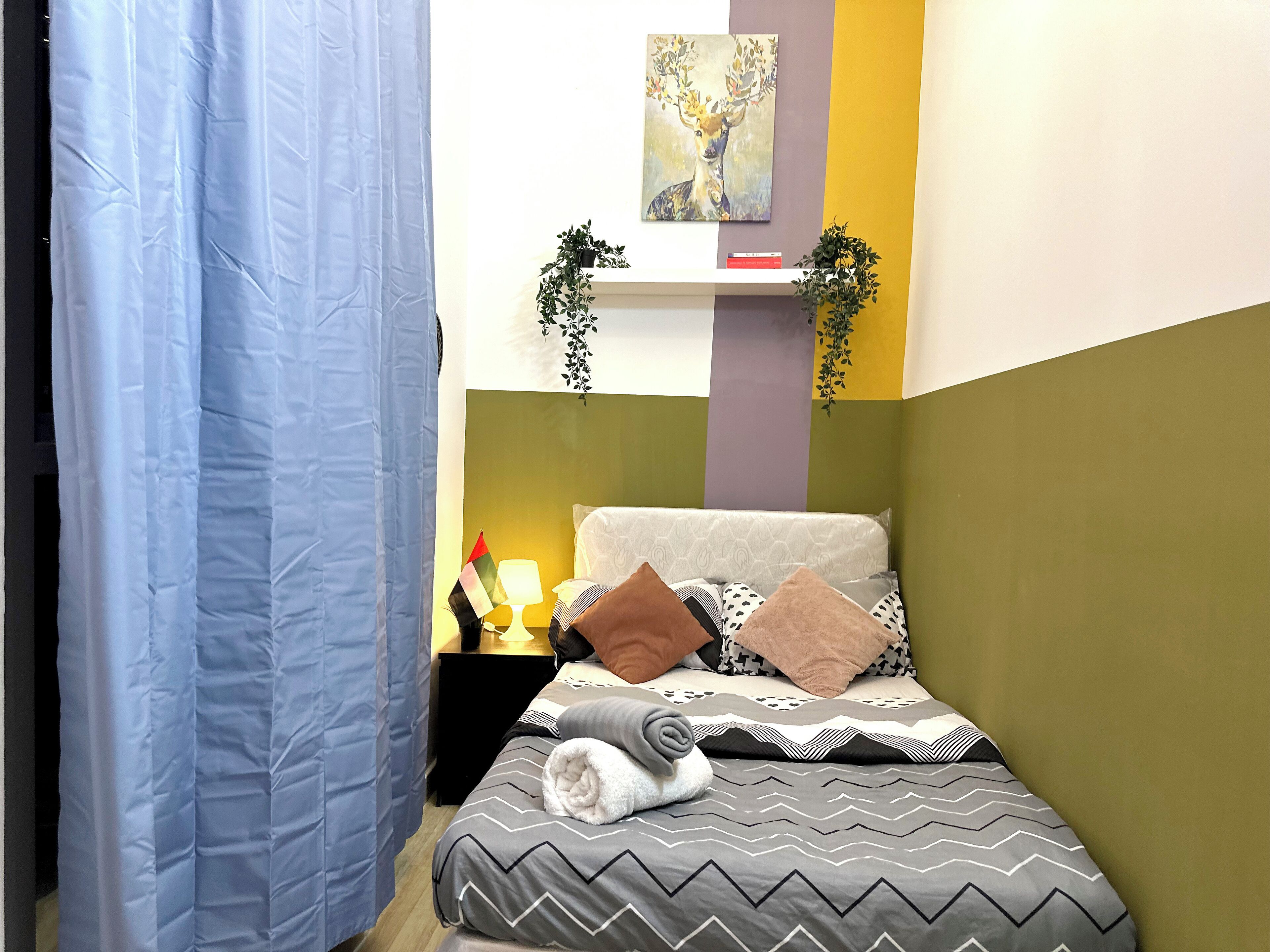 Une chambre à coucher bien rangée, avec un lit, des oreillers, une table de chevet avec une lampe et un tableau accroché au mur.
