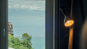 Habitació amb un gran finestral que donava a una massa d'aigua i un edifici. Hi ha una làmpada de peu de fusta amb llum encès.