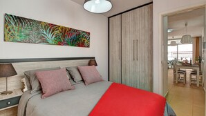 A modern bedroom with a bed, a colorful abstract painting, a wardrobe, and a dining area visible through an open door. - Muellito Playa - Puerto Naos (Puerto de Naos)