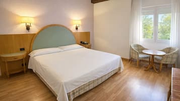 Habitación de hotel con cama, mesitas de noche, una silla, una mesita pequeña y una ventana con cortinas.