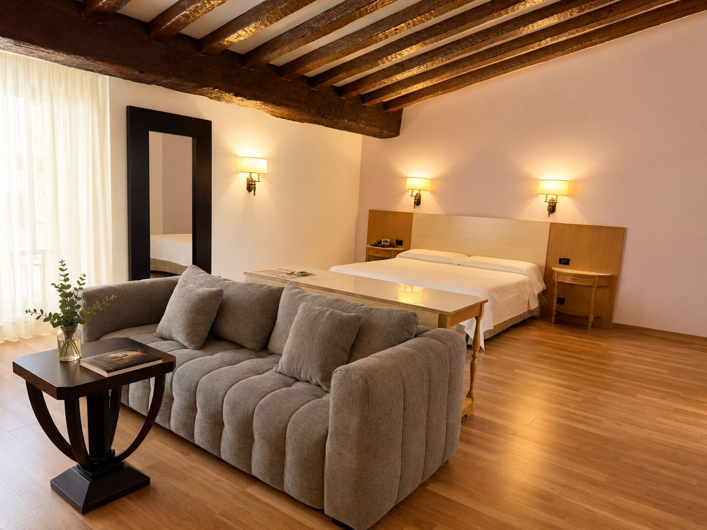 Una habitación de hotel con sofá, cama, mesitas de noche y lámparas de pared.