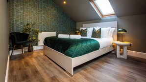 A modern bedroom with a sloped ceiling, a skylight, a bed with green bedding, a bedside table with a lamp, and a chair. - Luxury apartment & terrace view over river & easy access to City Centre & Castle (Inverness)