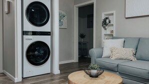 Una sala de estar moderna con un sofá gris, una mesa de centro redonda de madera y una lavadora y secadora de carga frontal.