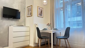 Ett litet rum med ett vitt skrivbord, två stolar, en platt-TV som är monterad på väggen och två inramade konstverk.