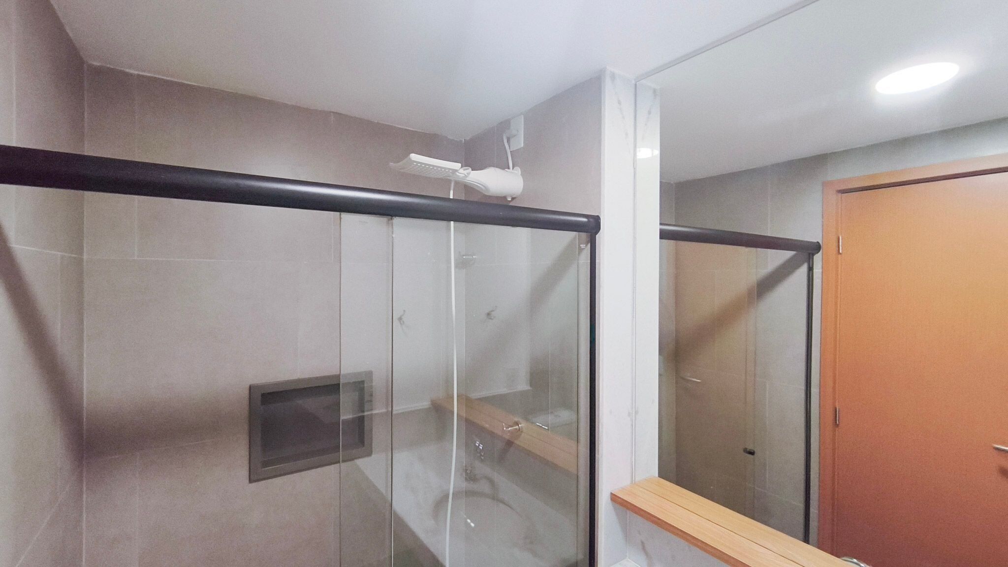 A modern bathroom with a glass shower enclosure, a wooden bench, and a visible towel rack.