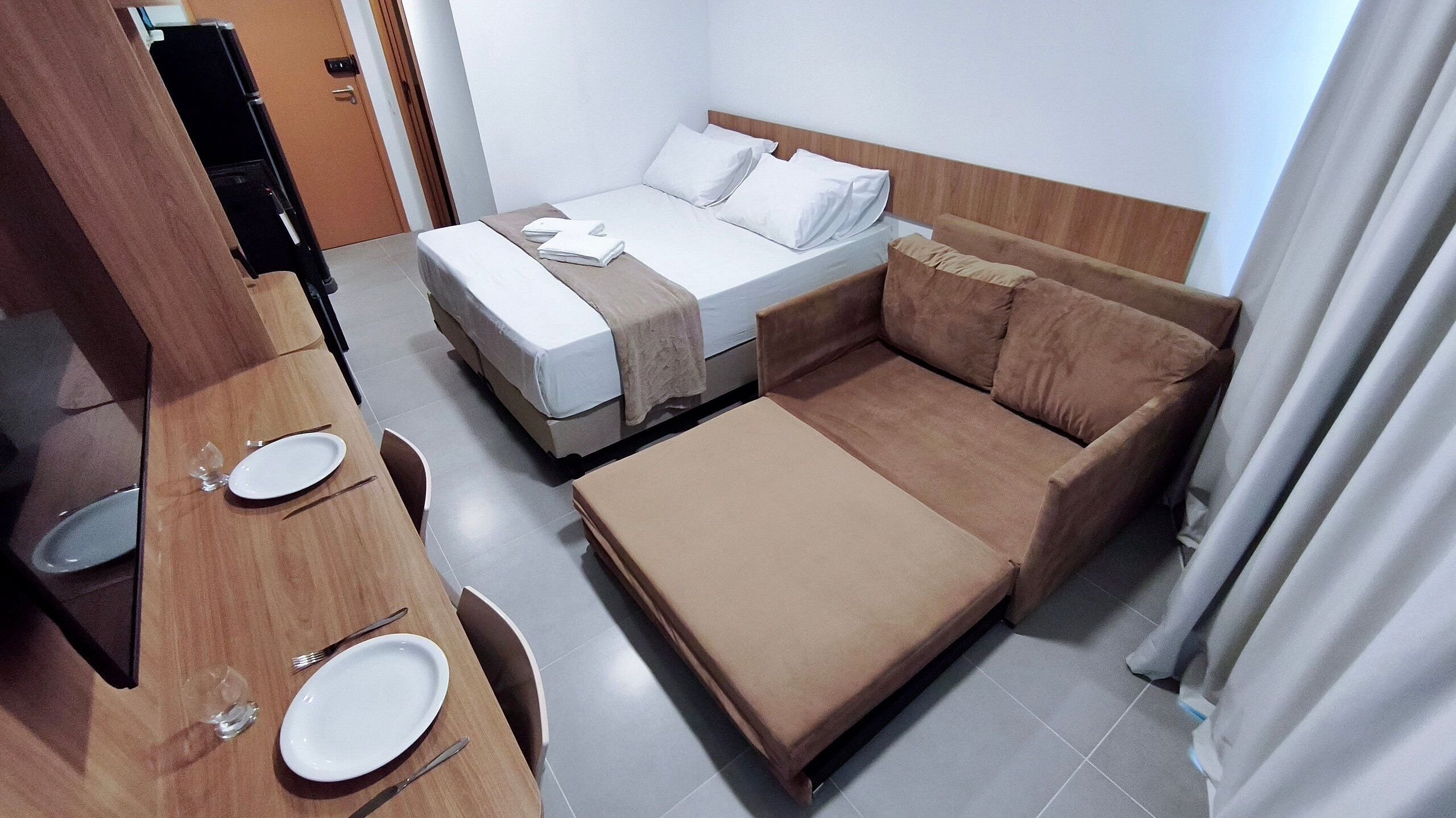 A hotel room with a bed, a sofa, a desk with a chair, and a television.