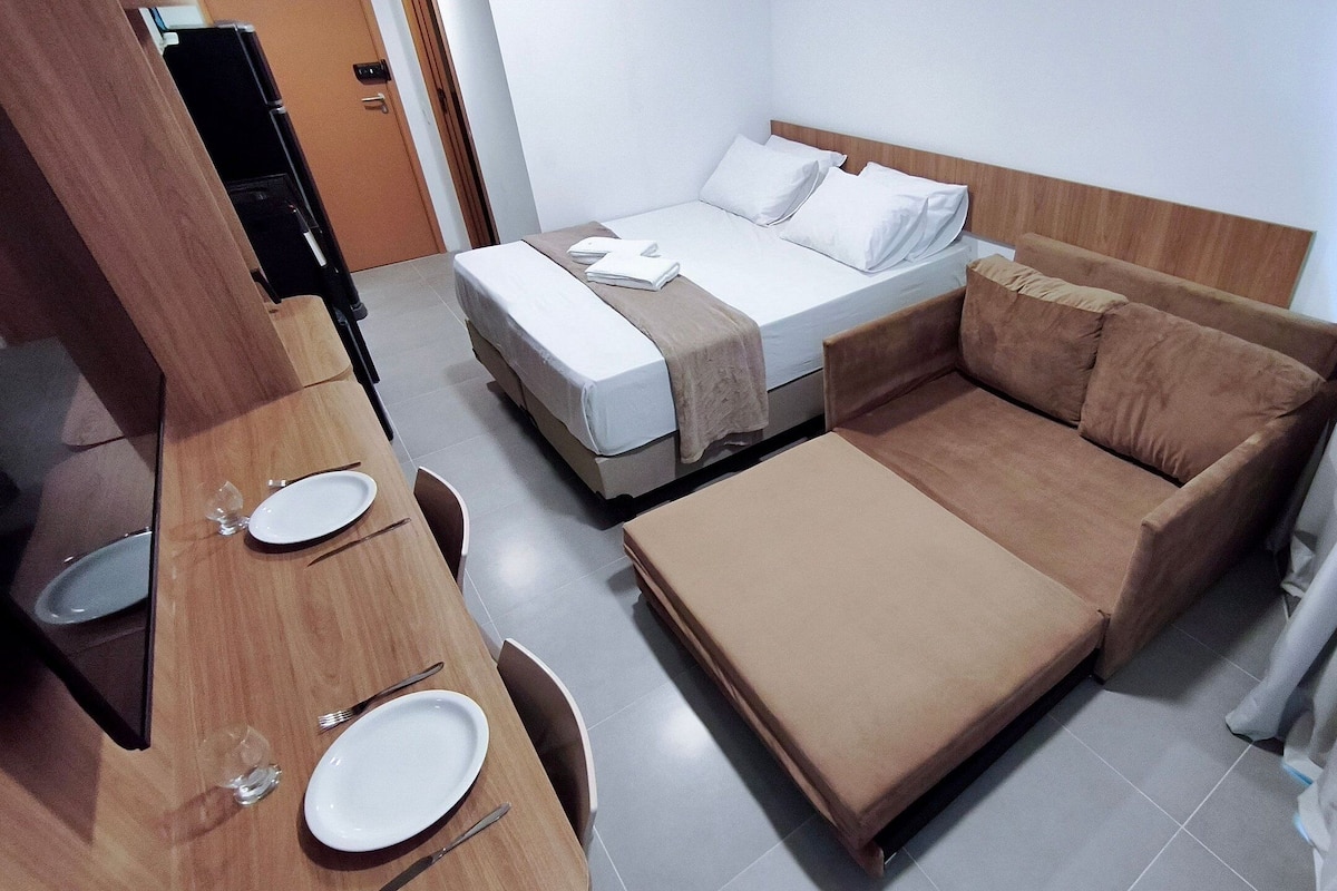 A hotel room with a bed, a sofa, a desk with a chair, and a television.