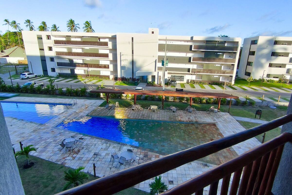 A rooftop pool area with lounge chairs, a pergola, and a view of modern buildings.