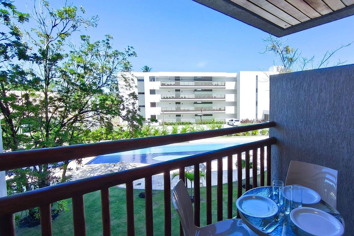 A balcony with a table set for dining, a pool, and a building in the background.